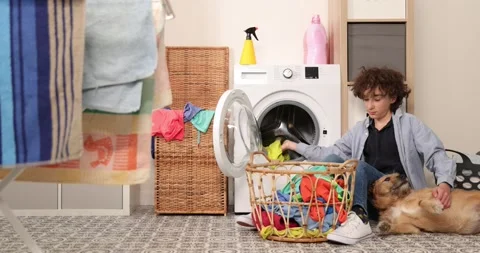 Housework. Boy doing laundry at home loading clothes into washing machin and Stock Footage 178432032