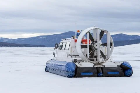 A hovercraft glides effortlessly over a snow-blanketed lake, surrounded by a Stock Photos