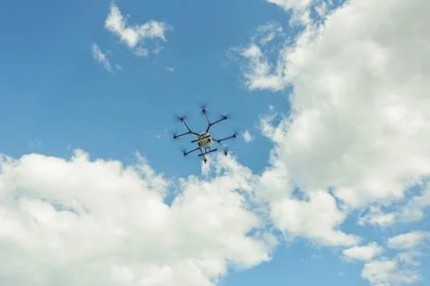 Hovering drone flies in blue sky and taking pictures of green hills. Stock Photos