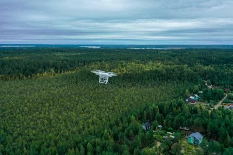 Hovering drone in the white sky over the forest, blue sky with w Stock Photos