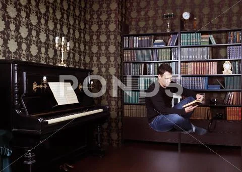 Hovering Man Reads Book In Room With Shelves, Piano And Brown Wallpapers