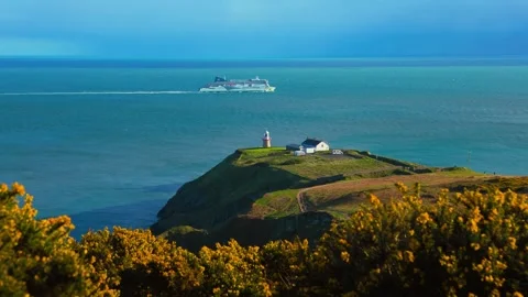 Howth Lighthouse with Stena Line Ferry Passing Calm Blue Sea and Gorse Flowers 스톡 동영상 333898582