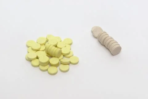 Huddle of yellow tablets with parting lines and neat stack of beige pills Stock Photos