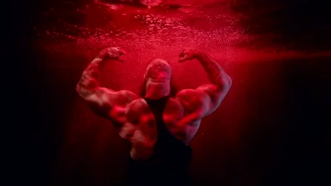 A huge bald man raised hands and poses with back in the dark water. red light Stock-Footage 183840482
