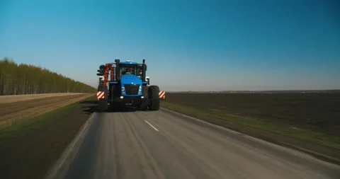 A huge blue tractor is driving down the road towards field for soil preparation. Stock Footage 240005054
