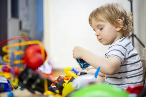 A huge bunch of different and colored toys in front of playful child. Little  Stock Photos