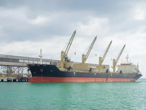 A huge cargo ship with cranes on it is moored at sea to the pier Stock Photos