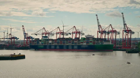 Huge Cargo Ship Moored at Container Terminal with Gantry Cranes and Windmills Stock Footage 345969795