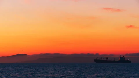 A huge cargo ship stands on a roadstead at sea in the yellow and red rays of sun Stock Footage 92205957