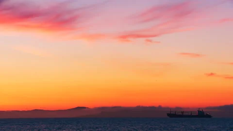A huge cargo ship stands on a roadstead at sea in the yellow and red rays of sun Stock Footage 92205965
