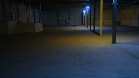 Huge empty warehouse aerial ascent as security worker walks through Stock Footage 107308476
