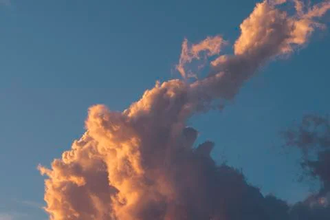 Huge expressive cloud in a light orange tint at sunset against a blue sky Stock Photos