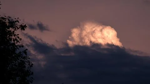 A huge fluffy cloud with a golden backlight from the sunset, towering over dark 스톡 사진