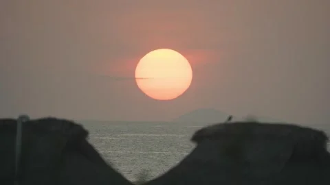 Huge golden sun disk sinking below the sea horizon with straw beach umbrellas Vídeo Stock 343435442