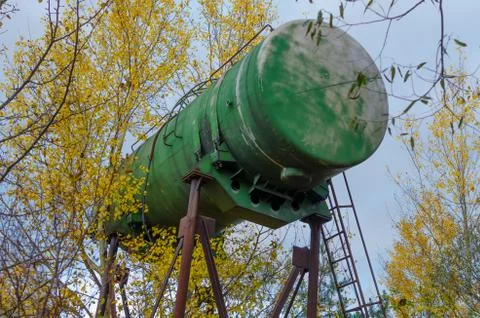 Huge green aluminium barrel on rusty metal support used as water tower. Stock Photos