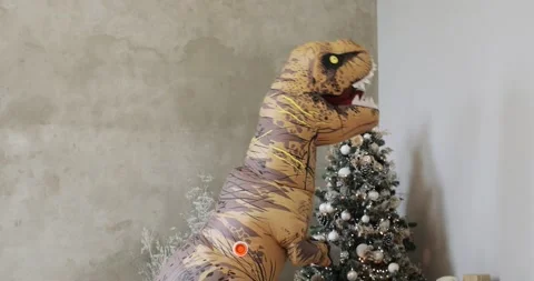 Huge inflatable dinosaur puts a gift near Christmas tree in New Year time. Stock Footage 143856273