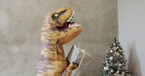 Huge inflatable dinosaur shaking gift box near Christmas tree in New Year time. Stock Footage 143843112