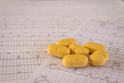 Huge orange-yellow pills on paper with EKGs and cardiac arrhythmias. Medicati Stock Photos