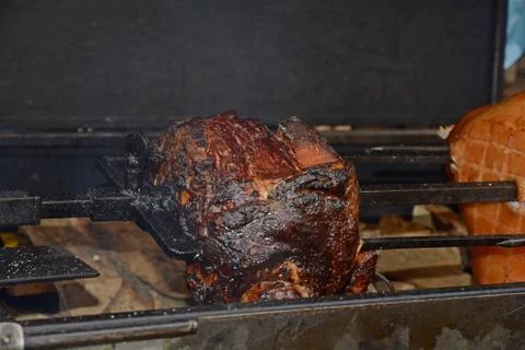 A huge pork ham is fried on a spit on the street. Stock Photos