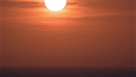 The huge red sun sets westward into the se Stock Footage 257056815