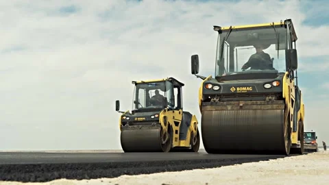 Huge road rollers of yellow colour drive along black highway Stock Footage 134460764