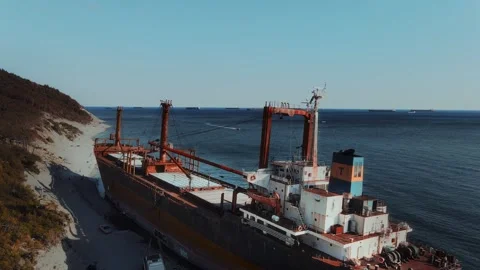A huge rusty cargo ship was washed up on a rocky seashore after strong waves Vídeos de archivo 330259922