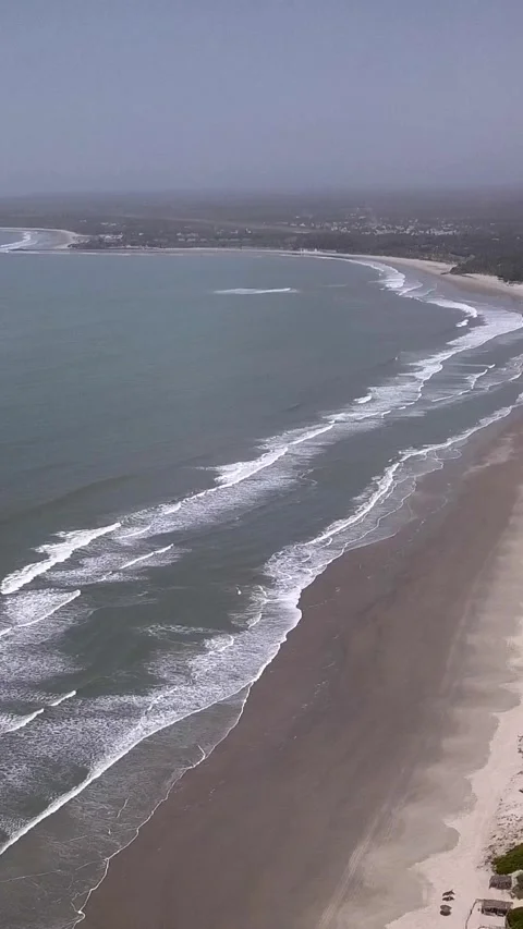 Huge sandy beach with waves crashing, vegetation and buildings along the coast Video stock 230670876