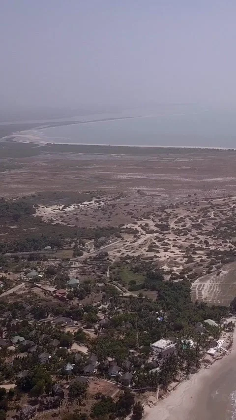 Huge sandy beach with waves crashing, vegetation and buildings along the coast Stock-Footage 230670974