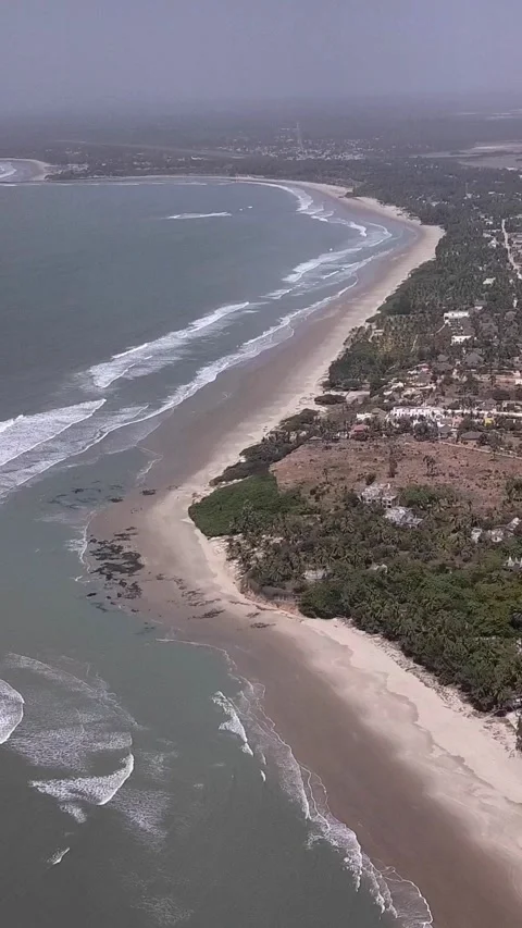 Huge sandy beach with waves crashing, vegetation and buildings along the coast Stock Footage 230671053