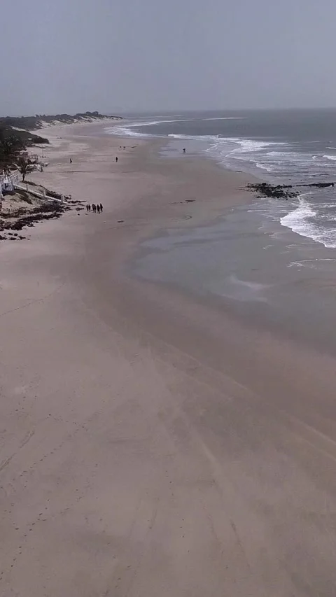 Huge sandy beach with waves crashing, vegetation and buildings along the coast Stock Footage 230671291