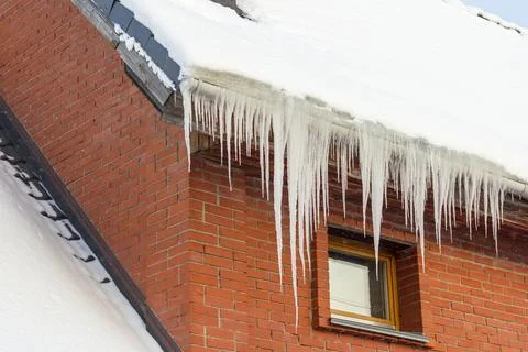 Huge sharp icicles of ice hang from the roof of a residential building. Stock Photos