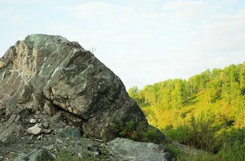 A huge stone boulder on a hillside overlooking the mountain taiga in the even Stock Photos