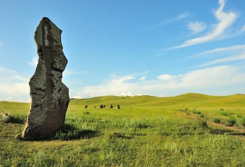 A huge stone menhir standing in the center of a vast meadow surrounded by hil Stock Photos