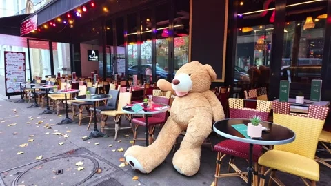 Huge Teddy bear sitting alone at outdoor café terrace in public space, Paris Stock Footage 325718561