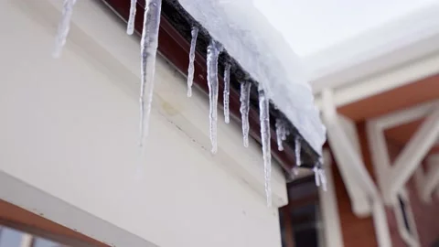 Huge thick icicles hanging from the roofs are melting under the spring sun Stock Footage 145735536