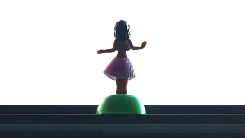 A hula dancer dancing in front of a window. Toy wiggler seen from the back. Stock Footage 146098388