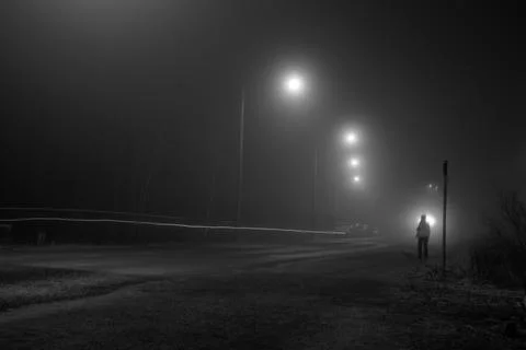 Human alone standing in front of white street lights in foggy night. Dark t.. Stock Photos