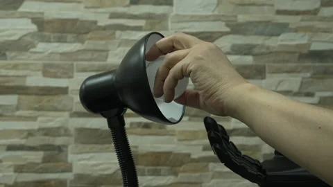 Human and Robotic or Prosthesis Hand Changing Light Bulb in Desk Lamp Stock Footage 340578824
