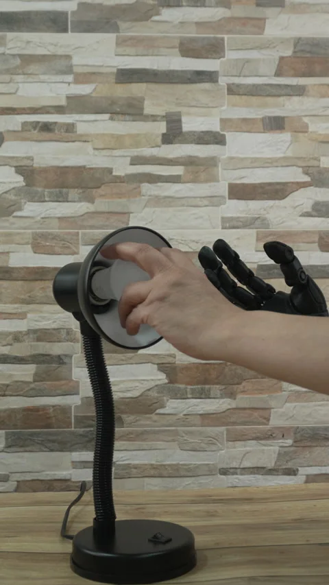 Human and Robotic or Prosthesis Hand Changing Light Bulb in Desk Lamp Stock Footage 341175395