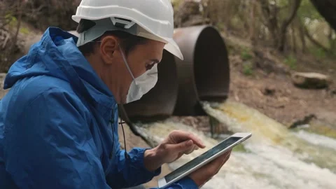 A human ecologist, an engineer wearing a helmet and a respirator, uses a tablet Video stock 132207923