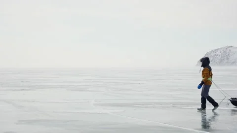 Human with equipped sledge moving across frozen ice. Snowy misty gray scenery Stock Footage 165839619