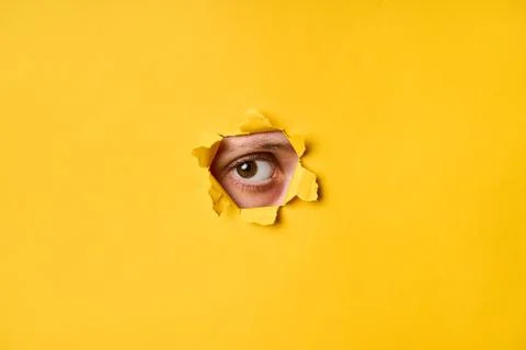 Human eye looking through torn yellow paper Foto stock