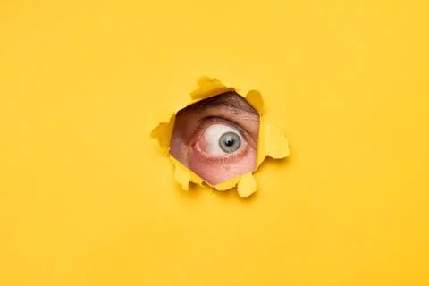 Human eye looking through torn yellow paper Foto stock