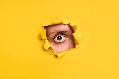 Human eye looking through torn yellow paper Stock-Fotos