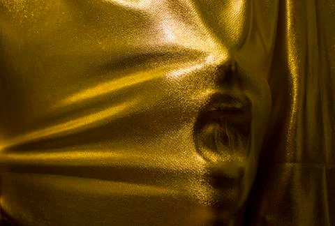 Human face pressing through golden fabric Stock Photos
