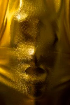 Human face pressing through golden fabric Stock Photos