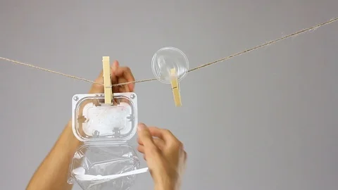 Human fasten plastic utensils by clothespin to rope, disposable tableware reuse Stockbeeldmateriaal 112366756