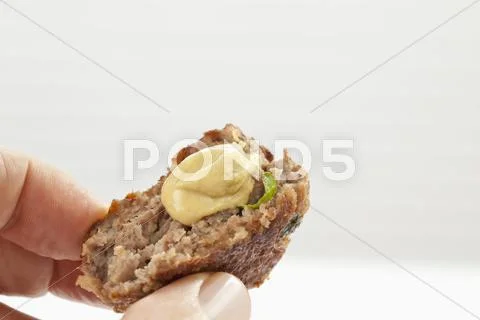 Human finger holding fried minced pork patties with mustard, close up Stock Photos