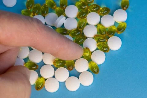 Human finger sorting white tablets and yellow capsules on blue background Foto stock