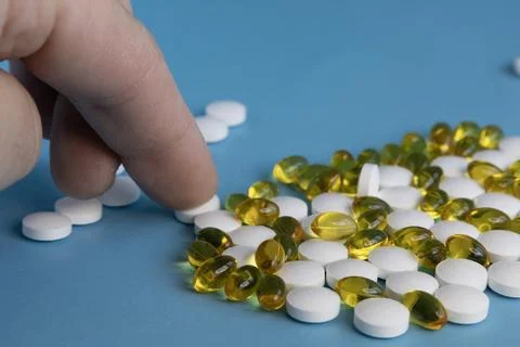 Human finger sorting white tablets and yellow capsules on blue background Fotos de archivo